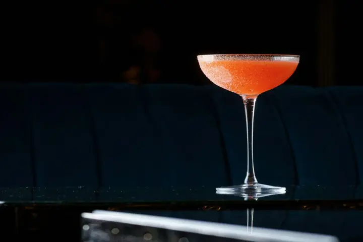 Orzeźwiający el presidente cocktail, z pomarańczowym odcieniem i cukrową obrączką, stoi na błyszczącym blacie.