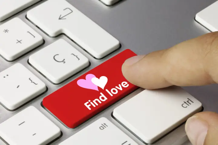 Palec naciska czerwony klawisz z sercami i napisem "Find love", symbolizując bezpieczne randki online.