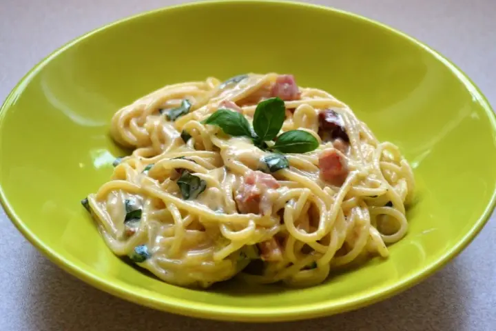 Spaghetti carbonara ze śmietaną, podane w zielonej misce, udekorowane bazylią. Pyszny przepis na klasyczne danie.