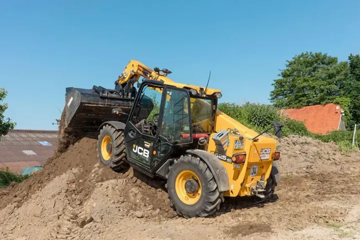 Żółty ładowarka teleskopowa JCB 525-60 z podniesionym wysięgnikiem i łyżką, pracująca na budowie.