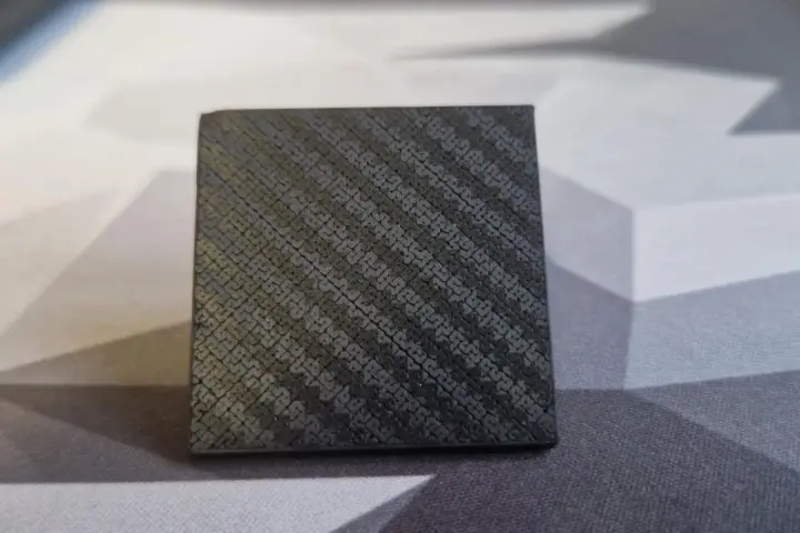A small cube with a textured surface, showcasing the intricate pattern achieved through carbon fiber 3D printing.