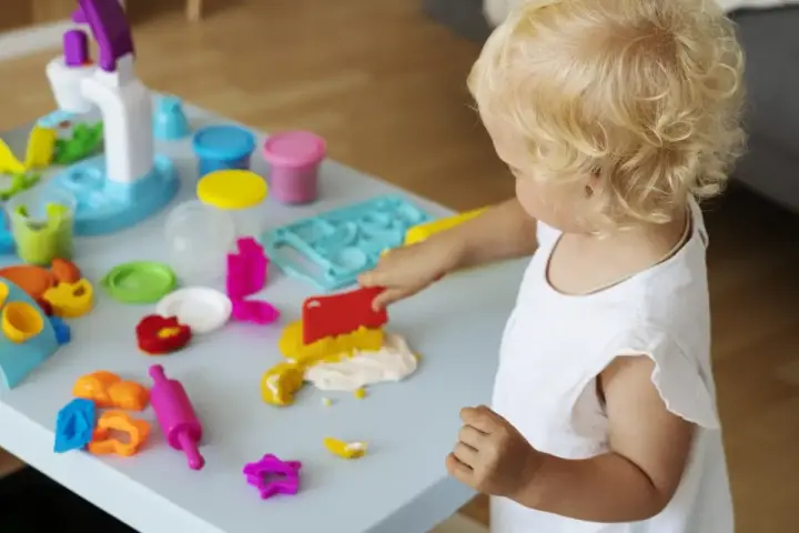 Małe dziecko z blond włosami bawi się masą plastyczną, wspierając swój rozwój sensoryczny.