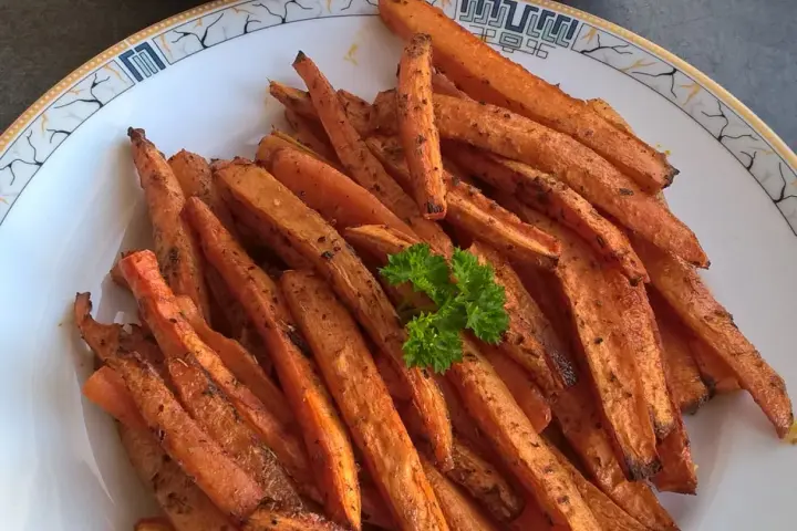 Stos pieczonych frytek z marchewki z natką pietruszki na talerzu.