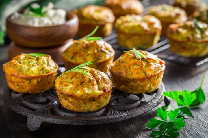 Deliziosi tortini di zucchine dorati, guarniti con rosmarino, su un piatto di ghisa. Sullo sfondo, una ciotola di formaggio fresco.