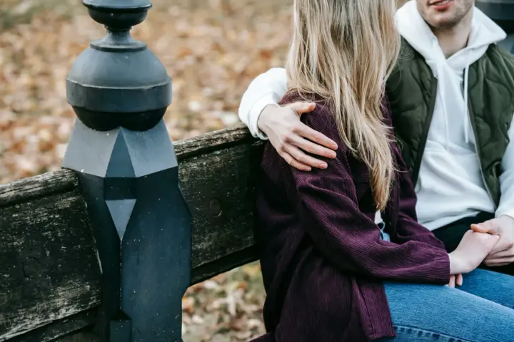 Un homme enlace tendrement une femme assise à ses côtés sur un banc. Un geste qui dit "comment dire je t'aime sans le dire".