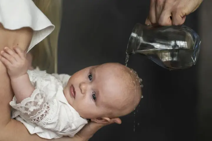 Chrzest chłopca: polewanie główki wodą z dzbanka.