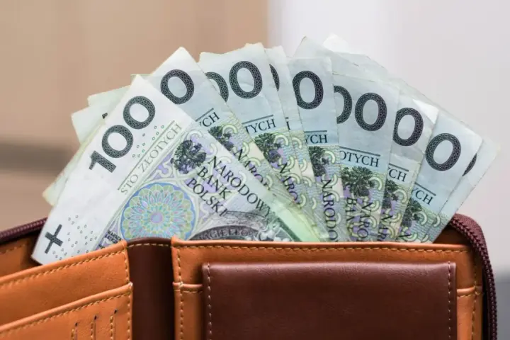 Portfel z banknotami 100 zł. Czy urlop wychowawczy jest płatny? To pytanie nurtuje wielu rodziców, a pieniądze w portfelu mogą pomóc w podjęciu decyzji.