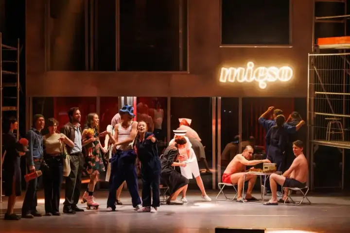 Scena z musicalu "1989". Aktorzy w strojach z epoki, neon "mięso" w tle.