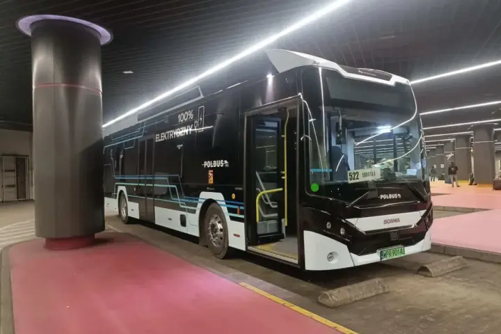 Nowoczesny, czarny autobus elektryczny z napisem "100% ELEKTRYCZNY" stoi na przystanku.