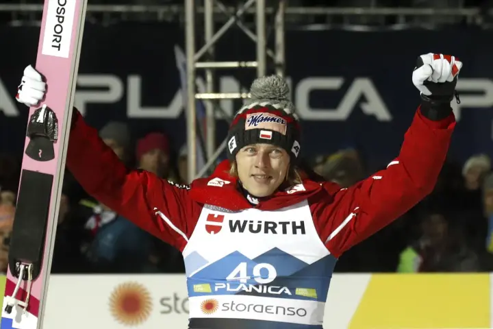 Skoczek narciarski w czerwonej kurtce i czapce z polską flagą świętuje zwycięstwo na skoczni. Mistrzostwa świata w skokach narciarskich.