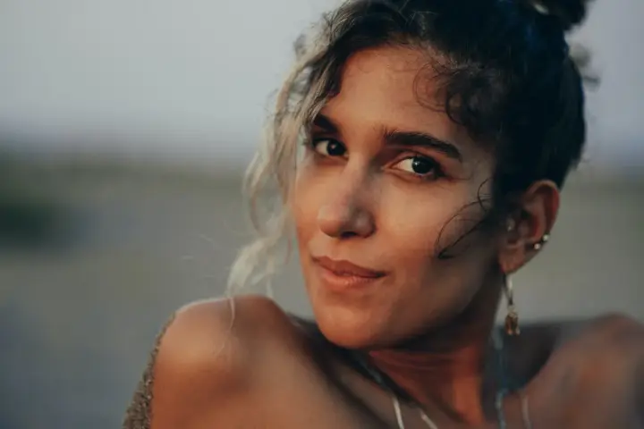 Photos de portrait d'une jeune femme aux cheveux bouclés, le sable sur son épaule, regardant la caméra avec un léger sourire.