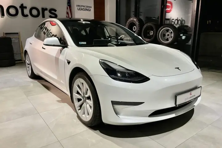 Biała Tesla Model 3 z napędem na cztery koła stoi w salonie samochodowym.