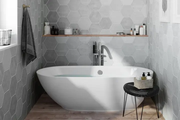 Salle de bain moderne avec baignoire îlot, carrelage mural hexagonal gris et étagère en bois.