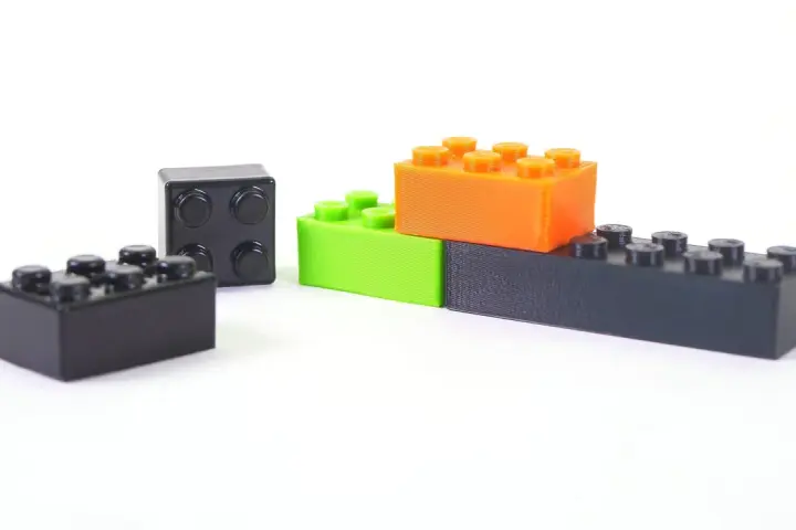 Klocki z drukarki 3D, wykonane z materiału ABS, w kolorach czarnym, zielonym i pomarańczowym, ułożone na białym tle.