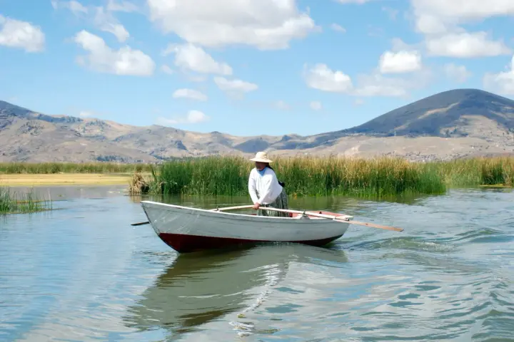 Donna con cappello di paglia rema su un lago, con montagne sullo sfondo. Mete agosto fuori Europa, un'immagine di pace.