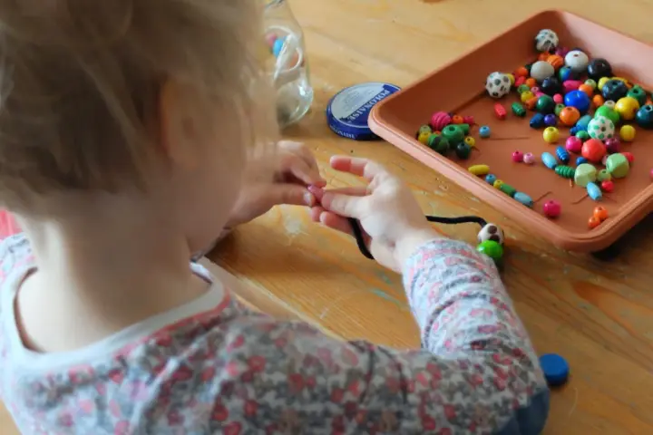 Dziecko uczy się, jak nawlec koraliki na sznurek, tworząc kolorową biżuterię.