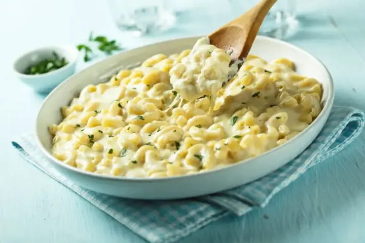 Kremowe makaronowe danie, idealne do przygotowania z przepisu na mac and cheese. Łyżka wydobywa porcję ciągnącego się sera.