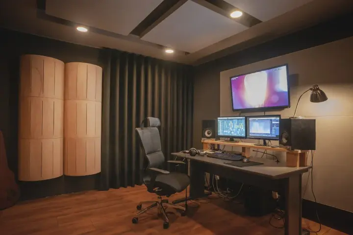 Studio nagraniowe z monitorem studyjnym, dwoma ekranami, wygodnym fotelem i panelami akustycznymi, które pomagają w kontroli **damping factor**.