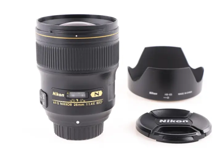 Obiektyw AF-S NIKKOR 28mm 1:1.4E ED z osłoną przeciwsłoneczną i deklem. Jasne oznaczenia obiektywów Nikon.