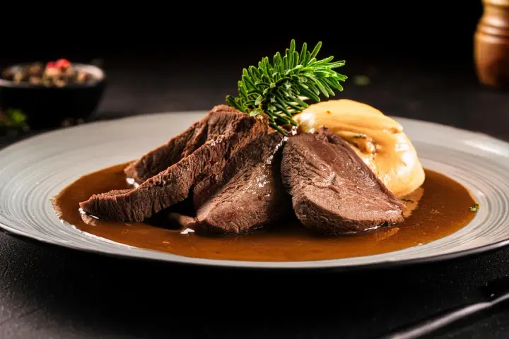 Zartes Tafelspitz-Rezept auf einem Teller mit Sauce, Beilage und Rosmarinzweig.