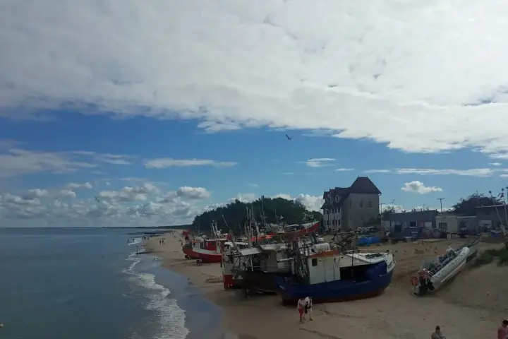 Chłopy trasa: łodzie rybackie na plaży, budynek z czerwonym dachem, morze i niebo z chmurami.