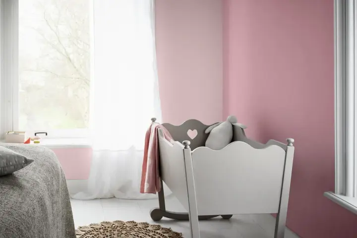 Pokój dziecięcy z łóżeczkiem, pluszowym królikiem i kocem w kolorze amarant. Ściany pomalowane na delikatny róż.