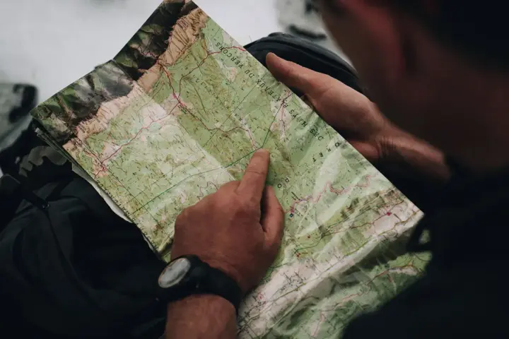 Un randonneur consulte une carte IGN des plateaux du Vercors, pointant un chemin sur le terrain.
