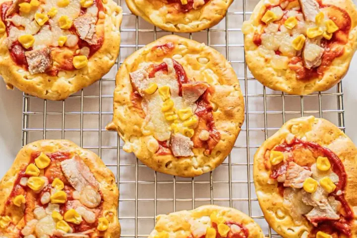 Mini pizze z serka wiejskiego, z kukurydzą i kawałkami mięsa, na metalowej kratce.