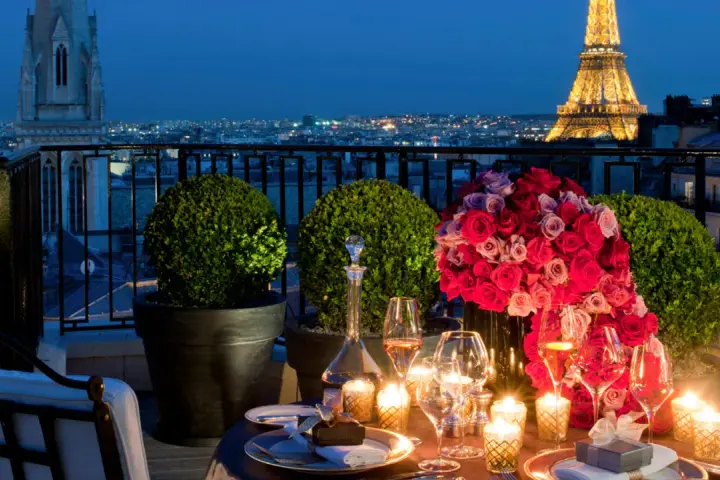 Cena romántica en París para San Valentín. Mesa con rosas, velas y Torre Eiffel iluminada al fondo.