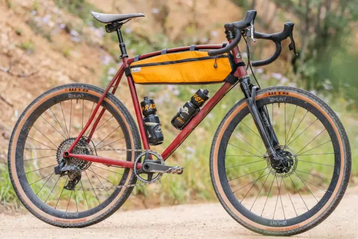 A red gravel bike with an orange frame bag and two water bottles. This bike, like many gravel bikes, does not have suspension, relying on its tires and frame for comfort.