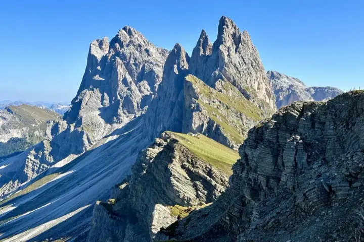 Majestätische Felszinnen ragen in den blauen Himmel. Eine **Seceda Wanderung** führt durch grüne Almwiesen und felsiges Gelände.