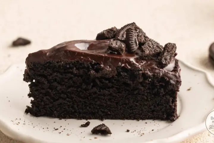 Ein saftiges Stück dunkler Oreo Kuchen mit glänzender Schokoladenglasur und zerbröselten Keksen obendrauf.