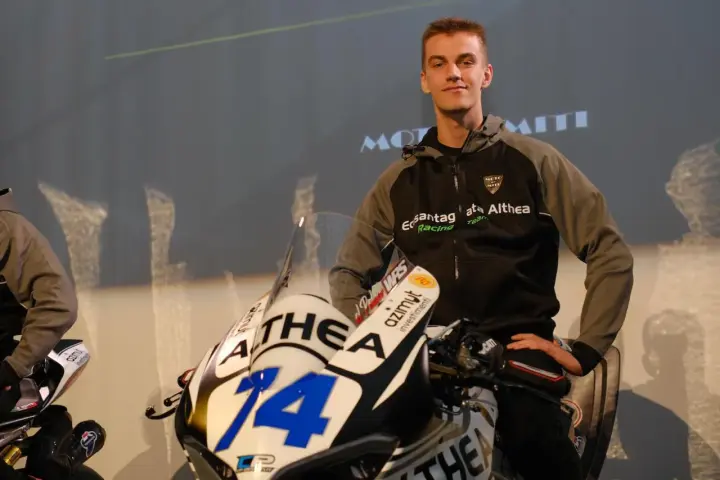 Piotr Biesiekirski, młody kierowca wyścigowy, pozuje obok swojego motocykla z numerem 14.