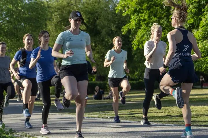 En grupp kvinnor tränar löpning utomhus. De springer i ett parkliknande område, redo att springa 1 km tid.