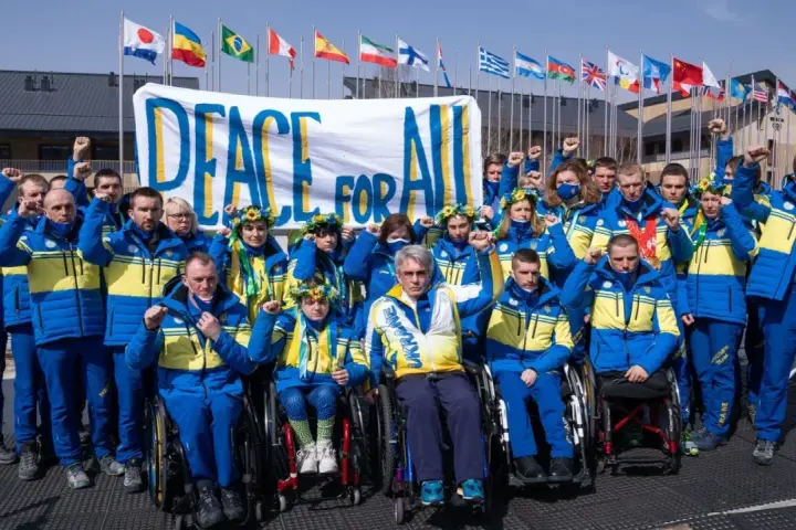 Ukraińska drużyna paraolimpijska z podniesionymi pięściami przed transparentem "Peace for All". Nadzieja na pokój na igrzyskach paraolimpijskich 2026.