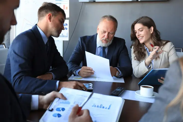Team discusses broker-dealer compliance, reviewing charts and documents in a meeting.