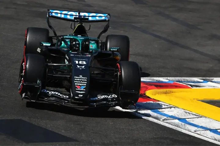 El coche de F1 Aston Martin número 18 se inclina en una curva, con sus neumáticos rozando la línea de la pista.