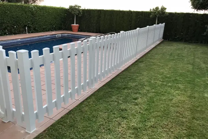 Una verja de jardín blanca protege una piscina y un césped verde.