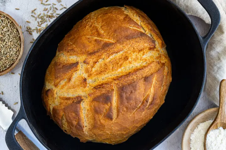 Ein goldbraunes Brot mit knuspriger Kruste liegt in einem Gusseisentopf. Dieses Brot kommt nicht aus dem Topf, sondern wurde darin gebacken.