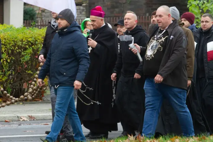 Grupa mężczyzn, w tym biskup, idzie ulicą. Niektórzy niosą różańce, jak rycerze Maryi.
