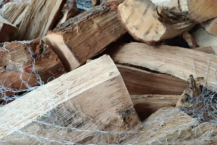Gros tas de bois humide, prêt pour le poêle. Les bûches sont emballées dans un filet blanc.