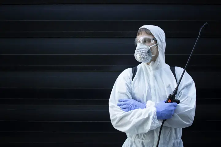Persona con traje protector, mascarilla y gafas, sosteniendo un pulverizador. ¿Cuánto tiempo esperar después de fumigar?