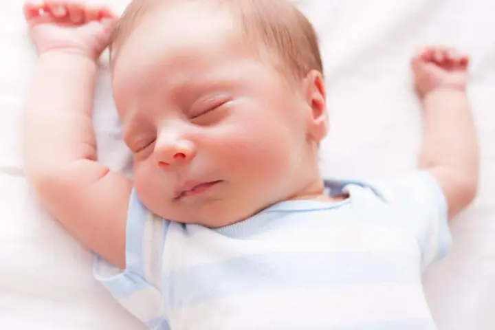 Un neonato dorme sereno con le braccia alzate. Sembra che i neonati possano mangiare mentre dormono, un vero miracolo della natura.