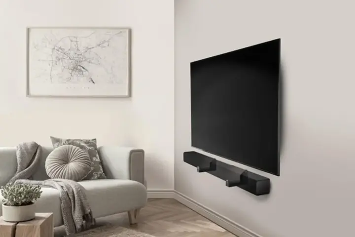 Un elegante soggiorno con un divano grigio e un quadro astratto. Al centro, un televisore a schermo piatto montato a parete con una soundbar nera.