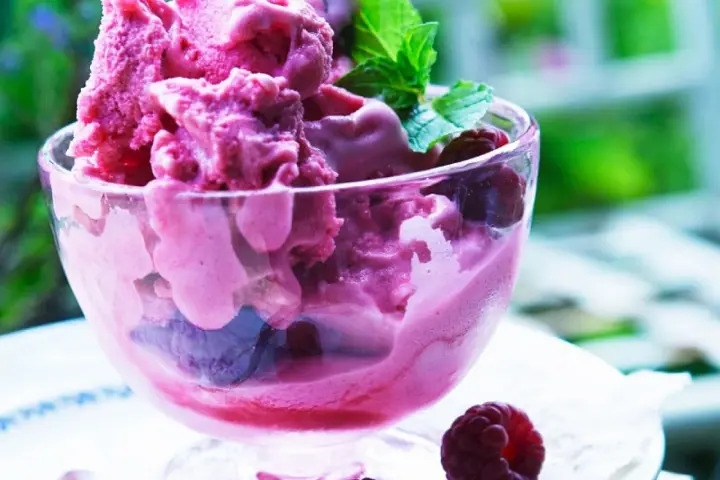 Himbeereis in einer Glasschale, frisch aus der Eismaschine, garniert mit Minze und ganzen Himbeeren.