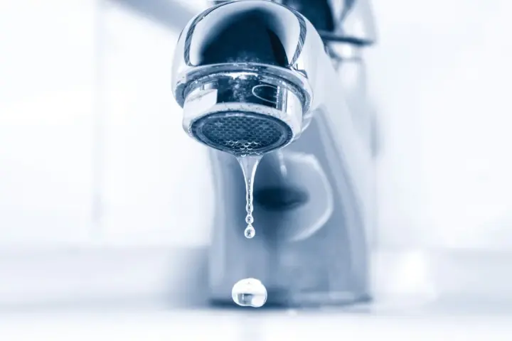 Gouttelettes d'eau tombant d'un robinet de salle de bain qui fuit. Un petit désagrément qui coûte cher.
