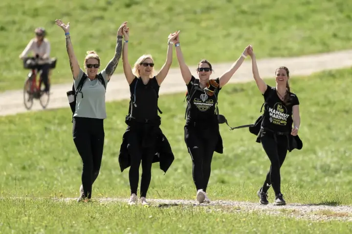 Cuatro mujeres celebran tomadas de la mano, con los brazos en alto, mientras caminan por un sendero. Su **velocidad media andando** parece alegre y enérgica.