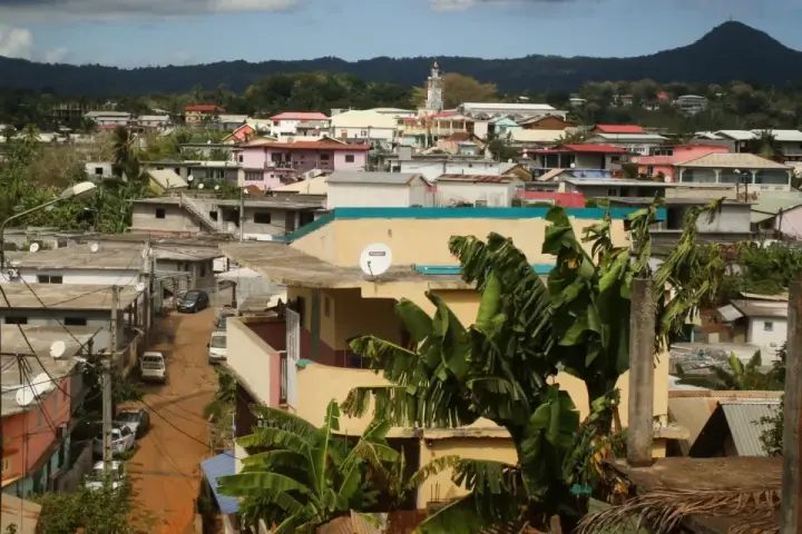 Vue d'une ville aux Comores, Mayotte, avec des maisons colorées, des bananiers et une montagne en arrière-plan.