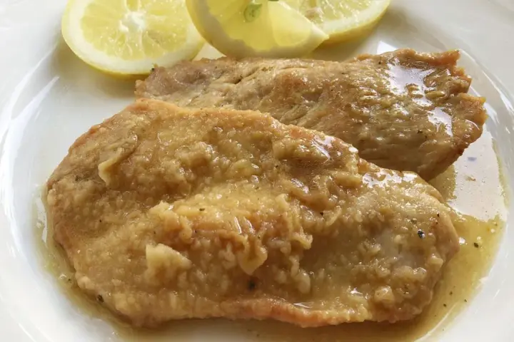 Deliziose scaloppine al limone, succulente e dorate, servite con spicchi di limone fresco.