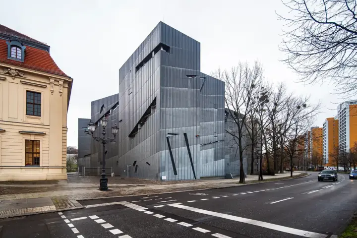 Nowoczesny budynek Muzeum Żydowskiego w Berlinie, obok zabytkowej kamienicy, z charakterystyczną, poszarpaną fasadą.